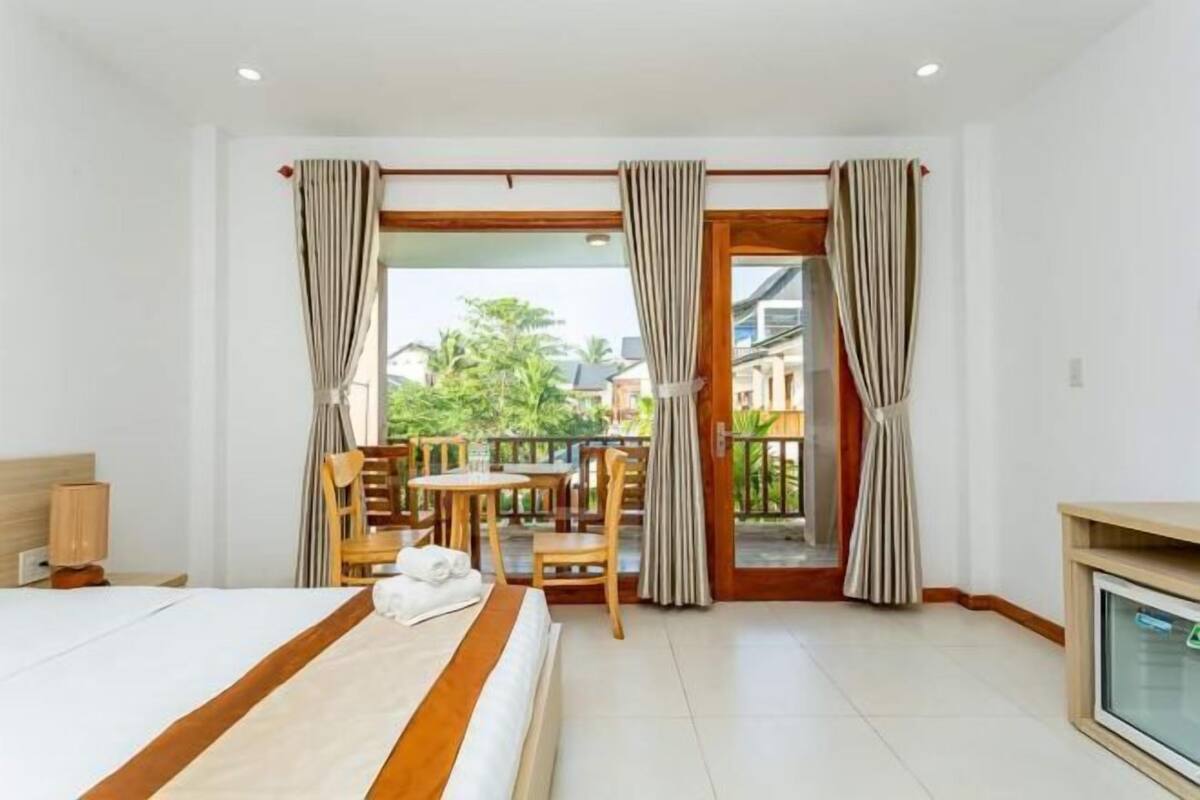 Une chambre d’hôtel équipée d’un lit, d’un bureau, d’une chaise, d’une télévision et d’un balcon avec des rideaux.