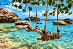 Eine Holzschaukel über klarem türkisblauem Wasser, im Hintergrund Felsformationen.