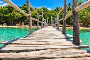 A wooden pier extending into clear turquoise water, supported by wooden posts and railings, with a tropical backdrop.