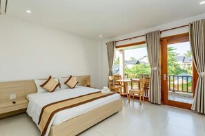 A hotel room with a bed, a table with chairs, and a view of the outdoors.