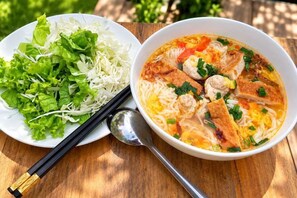 Eine Schüssel Suppe mit Nudeln und Fleisch, dazu ein Teller frisches Gemüse und ein Paar Essstäbchen.