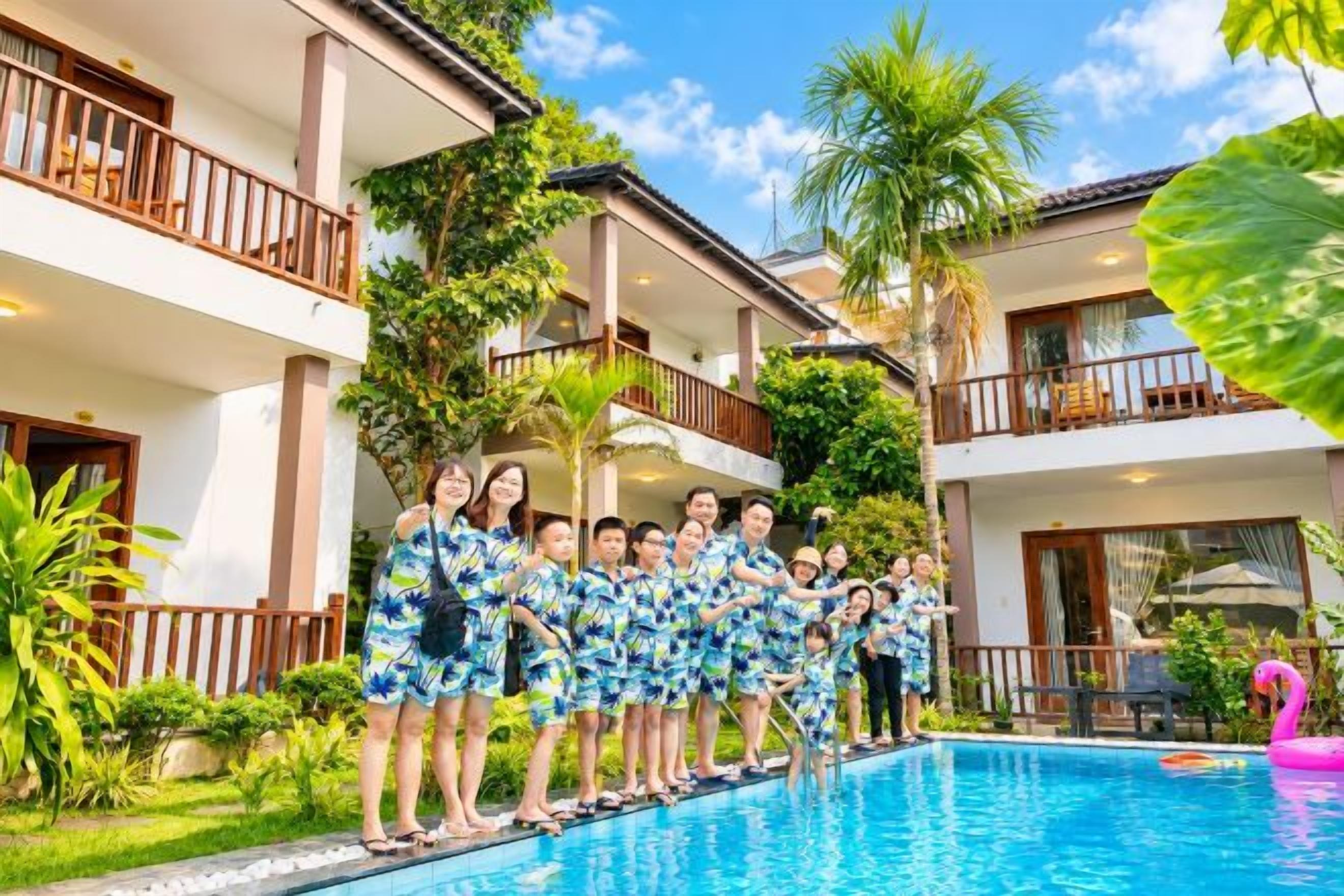 A group of people standing by a swimming pool with a building in the background.
