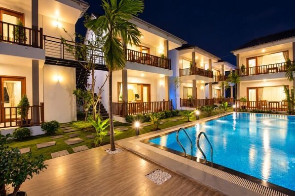 A multi-story hotel with a swimming pool, outdoor lighting, and a well-maintained garden.
