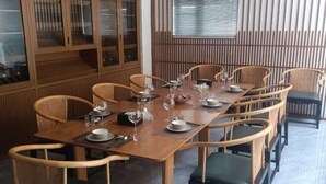 A dining area with a long wooden table, wicker chairs, and a cabinet with glass doors. - Good Luck Hostel (Phnom Penh)