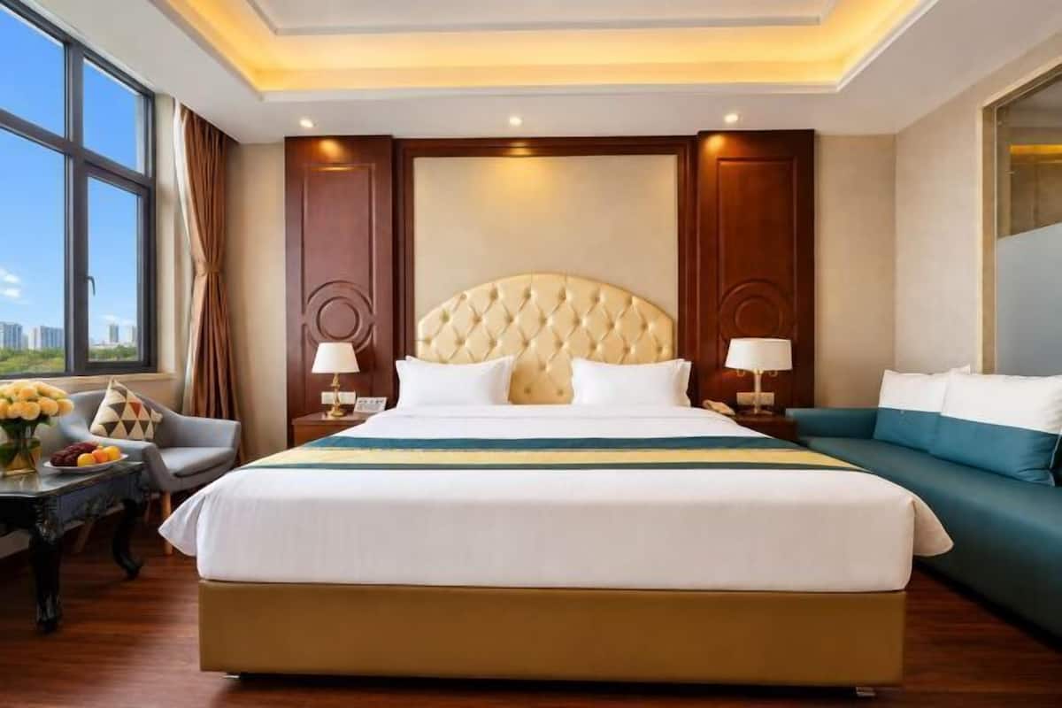 A hotel room with a large bed, a sofa, a desk with a lamp, and a view of the city.