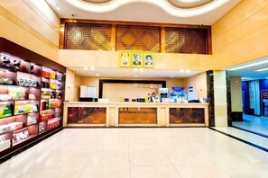 A hotel reception area with a modern design, featuring a reception desk, a seating area with magazines, and a decorative wall with geometric patterns.