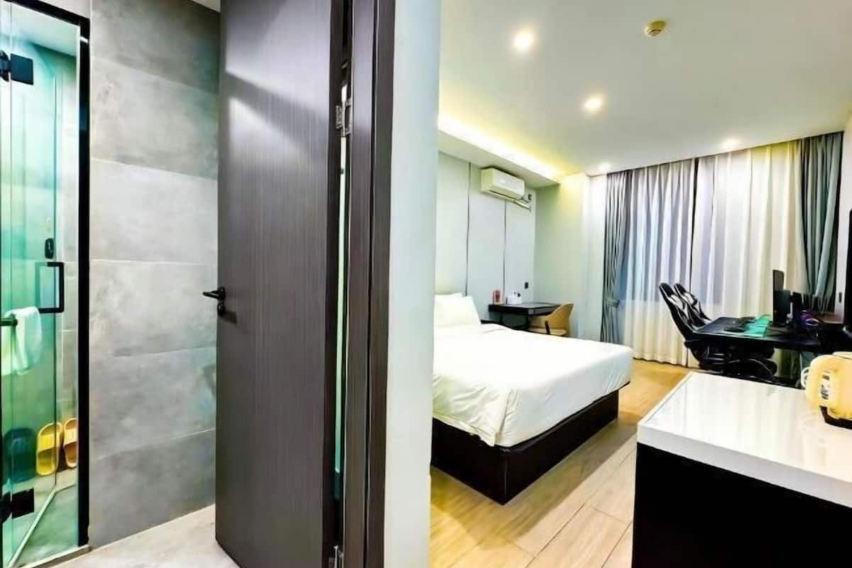 A hotel room with a bed, a desk, a chair, a glass shower enclosure, and a door.