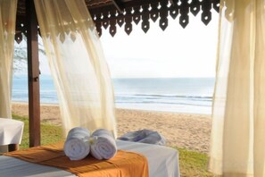 Una habitación frente a la playa con una cama, vista al océano y un dosel con adornos colgantes.