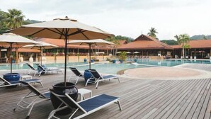 A poolside area with lounge chairs and umbrellas, surrounded by buildings with thatched roofs. - Club Med Cherating Beach (Balok)