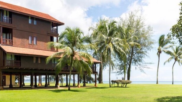 A two-story building with a red roof, surrounded by palm trees and a grassy area. - Club Med Cherating Beach (Balok)