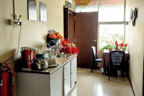 A kitchenette with a stove, sink, and various kitchen items. There is a dining table with chairs and a window with a view of greenery. - MB Hotel (Kota Kinabalu)