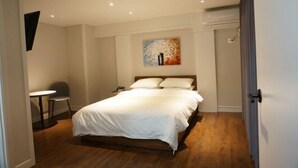 A bedroom with a bed, a small table, a chair, and a painting on the wall.