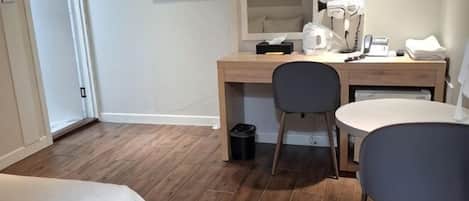Una habitación de hotel con cama, escritorio con silla, televisor, cafetera y cubo de basura.