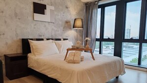 A modern hotel room with a large bed, a nightstand, a lamp, and a view of the city through large windows. - Pavillion Bukit Jalil 【Walk 2 mins】Stylish Lily Studio 2-4 Pax (Kuala Lumpur)
