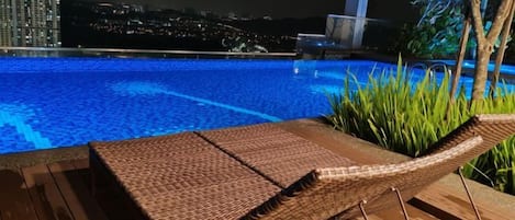 Un área de descanso con una silla de mimbre y vistas a una piscina por la noche.