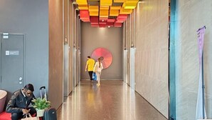 A hotel corridor with a modern design, featuring a large circular artwork on the wall and a seating area with a person using a laptop. - Pavillion Bukit Jalil 【Walk 2 mins】Stylish Lily Studio 2-4 Pax (Kuala Lumpur)