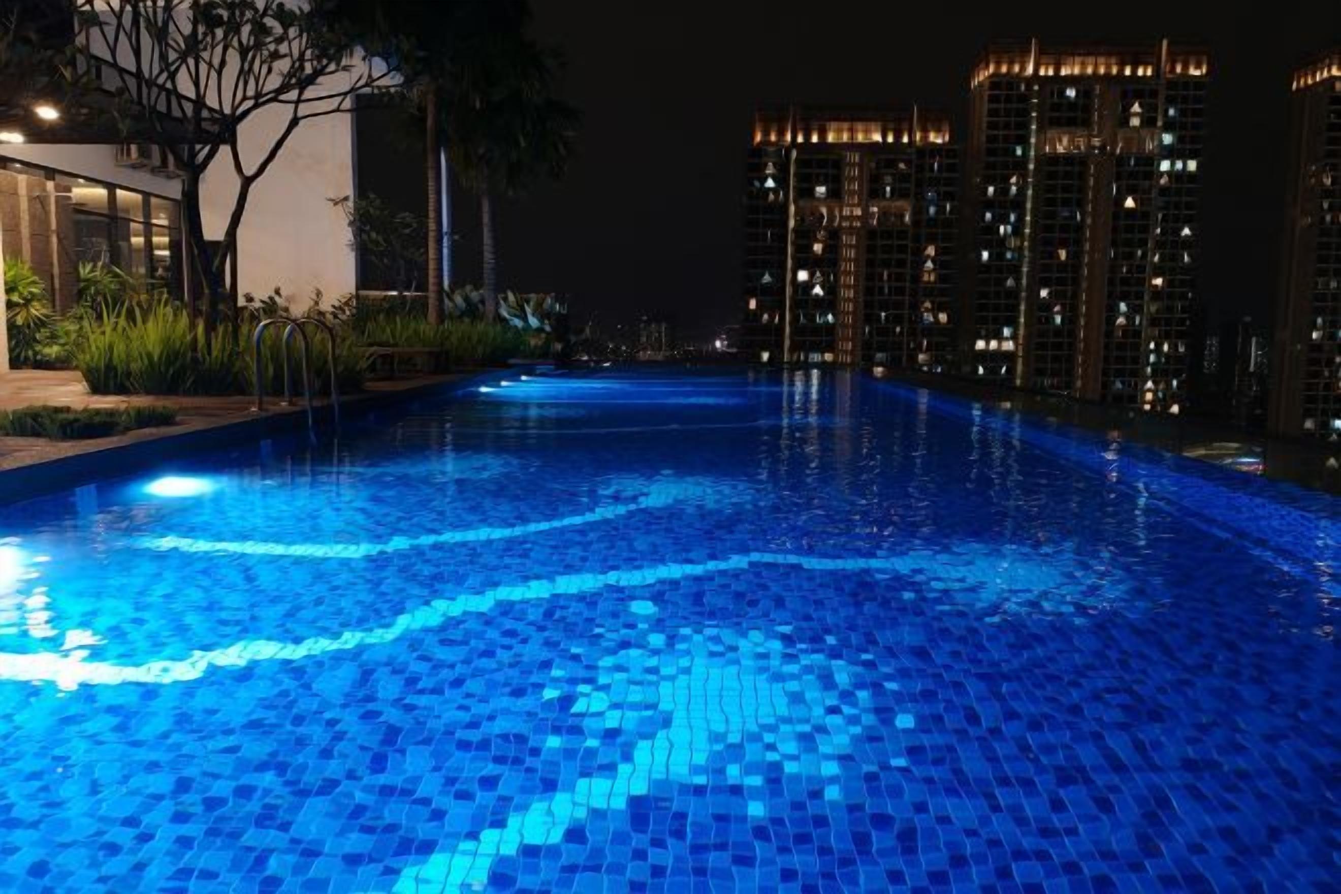 A swimming pool at night with illuminated tiles, surrounded by high-rise buildings.