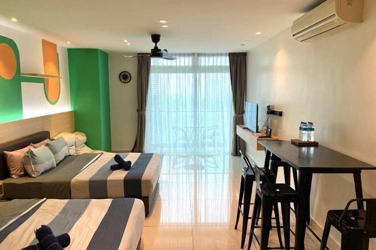 Ein Hotelzimmer mit zwei Betten, einem Schreibtisch, Stühlen, einer Klimaanlage und einem großen Fenster mit Vorhängen.