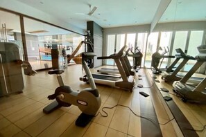 Une salle de sport équipée de divers appareils de cardio, dotée d’une grande fenêtre et d’un ventilateur au plafond.
