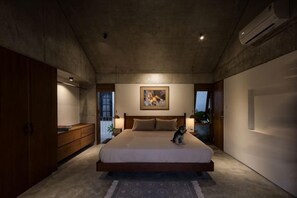 A bedroom with a large bed, a wooden wardrobe, a painting on the wall, and an air conditioning unit. - Private Nongnia Beach Villas (Hoi An)