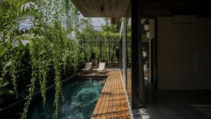 Uma área de piscina com deck de madeira, espreguiçadeiras e plantas penduradas.