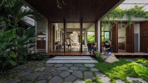 Uma casa moderna com fachada de vidro, caminho de pedra e vegetação exuberante.