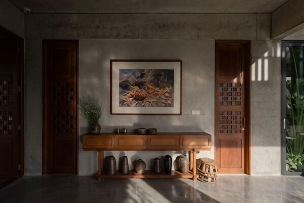 A room with a wooden console table, a framed painting, and a large wooden door.