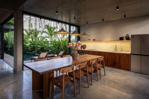 A modern kitchen with a wooden dining table, chairs, pendant lights, and a view of greenery outside. - Private Nongnia Beach Villas (Hoi An)