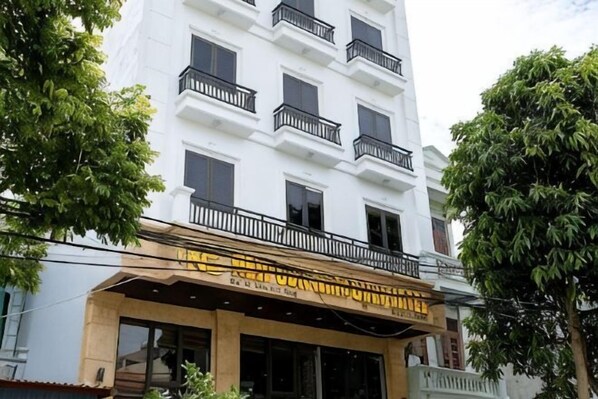 Un edificio de varios pisos con un balcón en la planta baja, ventanas amplias y un árbol en frente.