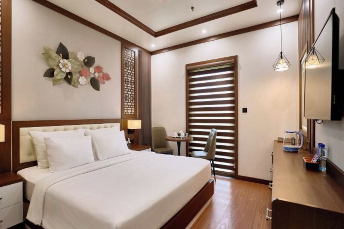 A hotel room with a large bed, a desk with a chair, a TV, and a window with blinds.