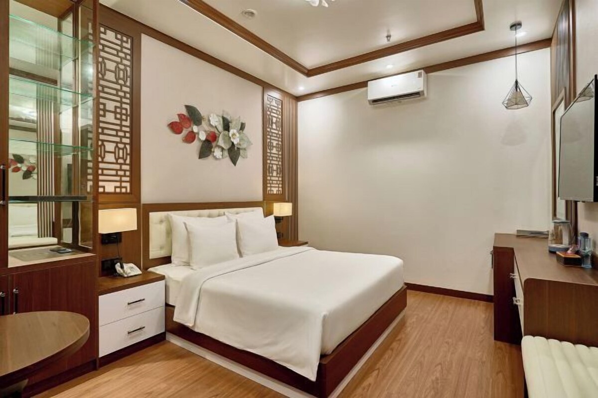 A hotel room with a bed, bedside table, lamp, decorative wall panel, and a mirror.