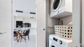 A modern laundry room with stacked washing machines and a basket. - 2-Bedroom Apartment Balcony Close to All Hotspots (MacGregor)