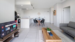 A modern living room with a grey sofa, a wooden coffee table, and a TV displaying a streaming service interface. - 2-Bedroom Apartment Balcony Close to All Hotspots (MacGregor)