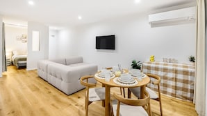 A modern living room with a sofa, a dining table set for four, and a TV mounted on the wall. - Spacious 2BR Getaway | Great Location & Comfort (Indooroopilly)