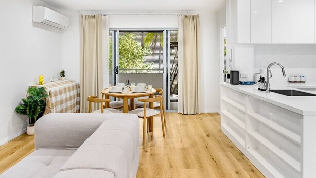A modern, well-lit room with a dining area, a sofa, and a kitchen with white cabinets and a sink. - Spacious 2BR Getaway | Great Location & Comfort (Indooroopilly)