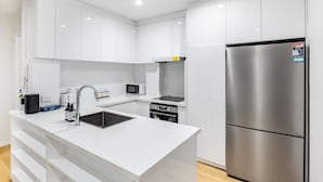 A modern kitchen with white cabinetry, a stainless steel refrigerator, a microwave, and an oven. - Spacious 2BR Getaway | Great Location & Comfort (Indooroopilly)