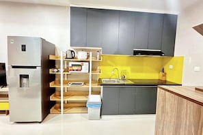 Een compacte keuken met een geïntegreerde koelkast, een houten plankunit en een gele achterwand.