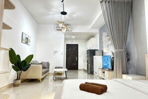 Ein modernes Hotelzimmer mit einem Bett, einem Schreibtisch, einem Stuhl, einer Pflanze und einer Küchenzeile.