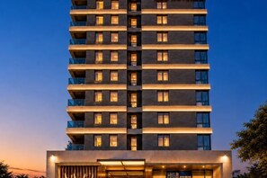 Un hotel moderno de gran altura, con varios pisos, balcones y una entrada bien iluminada.
