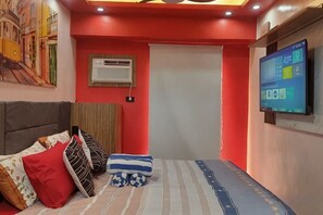 A bedroom with a bed, pillows, a television, and an air conditioning unit. - Near Manila Airport. Lovely "HOTEL STYLE" Studio Condo, With Kitchenette + Swimming Pool, 7A (Paranaque)
