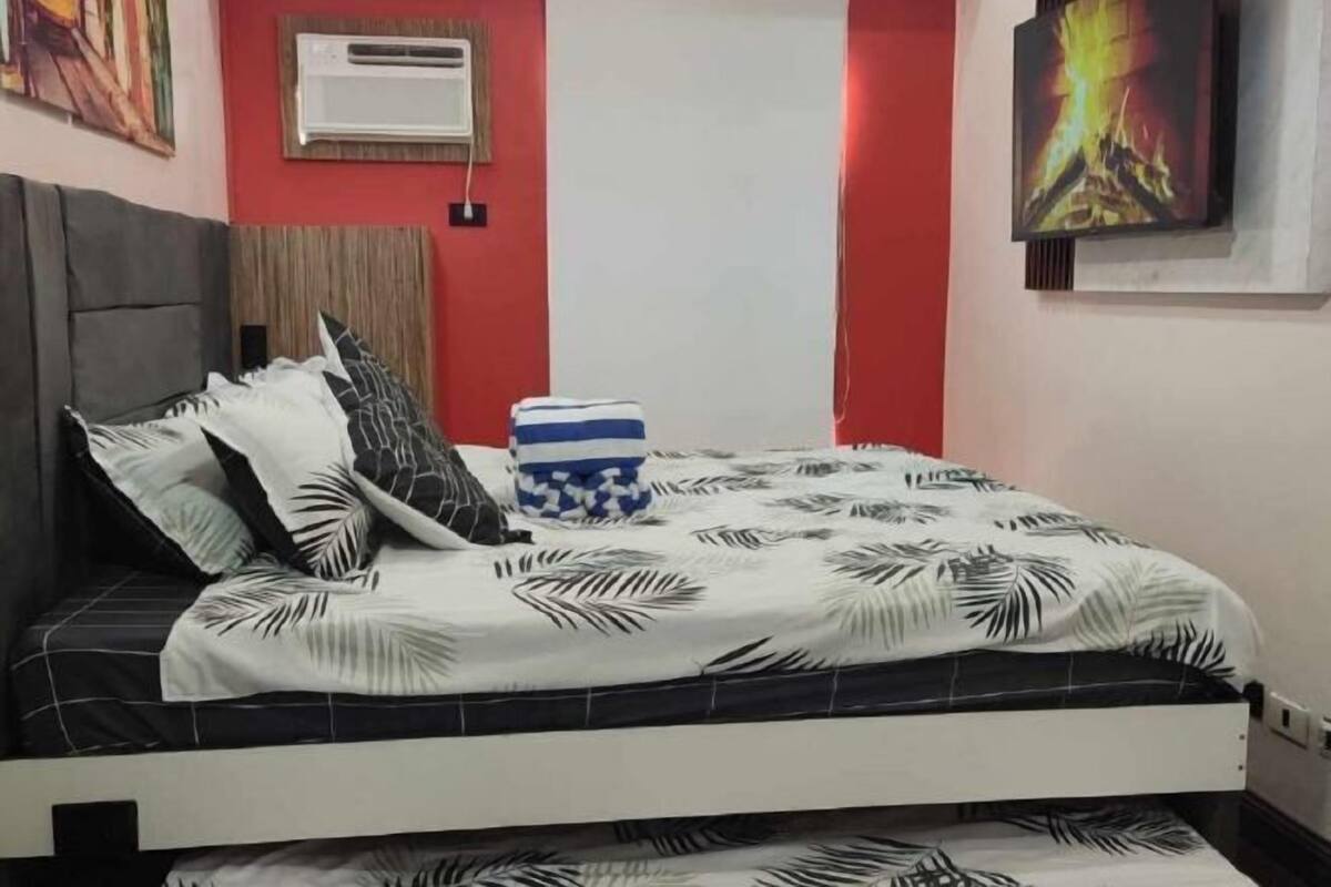 A bed with a patterned bedspread, a decorative vase, and a wall-mounted air conditioner.