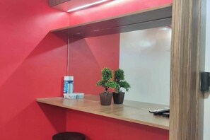 Una stanza con un parete rossa, uno scaffale di legno con una piccola pianta in vaso e un oggetto bianco sullo scaffale.