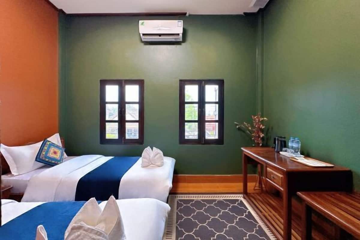A hotel room with two beds, a desk, a chair, an air conditioner, and two windows.