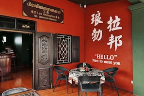 A room with a red wall, a table with chairs, and a door with a decorative panel. - Lao Hmong Hotel（Luang Prabang Old Town Center Store near JC Supermarket) (Luang Prabang)