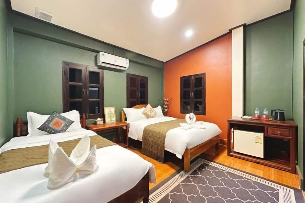 A hotel room with two beds, a small desk, a wardrobe, and a minibar.