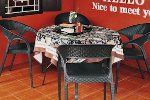 A round table with a floral tablecloth, surrounded by four wicker chairs, set against a red wall with partial text visible. - Lao Hmong Hotel（Luang Prabang Old Town Center Store near JC Supermarket) (Luang Prabang)