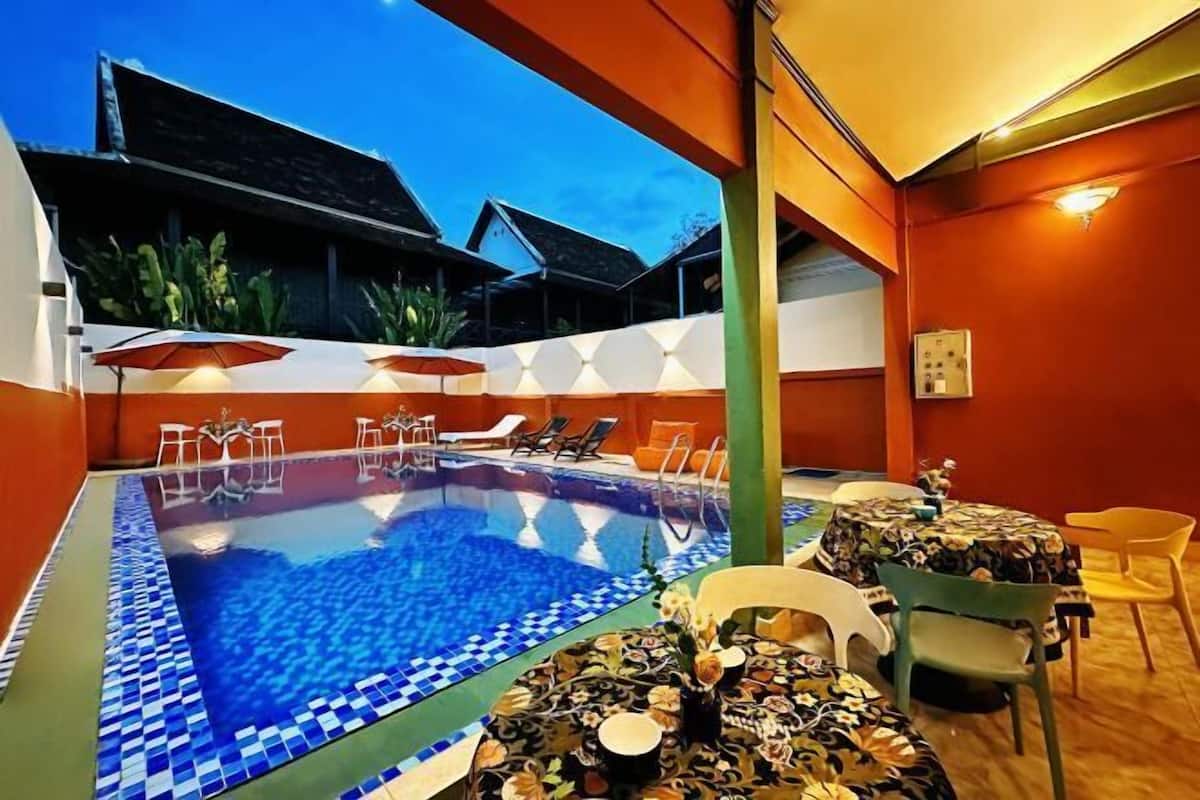 A swimming pool with lounge chairs and tables, surrounded by orange walls and a tiled floor.
