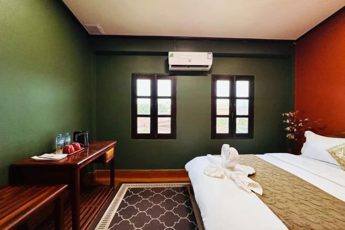 A hotel room with a bed, a desk with a chair, two windows, and an air conditioning unit.