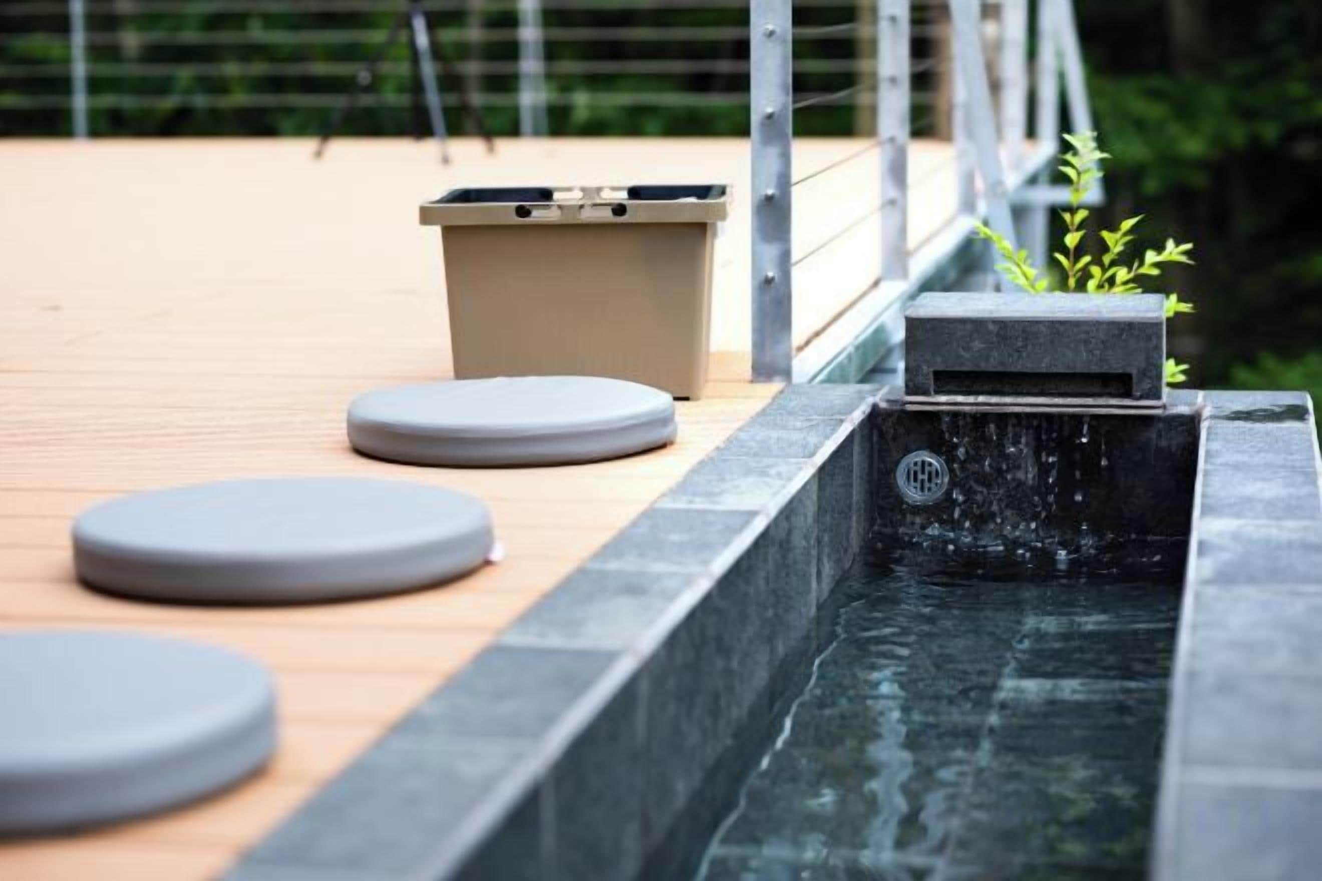 Uma cascata com uma pequena queda d'água, um deck de madeira e uma área de estar com banquetas circulares.