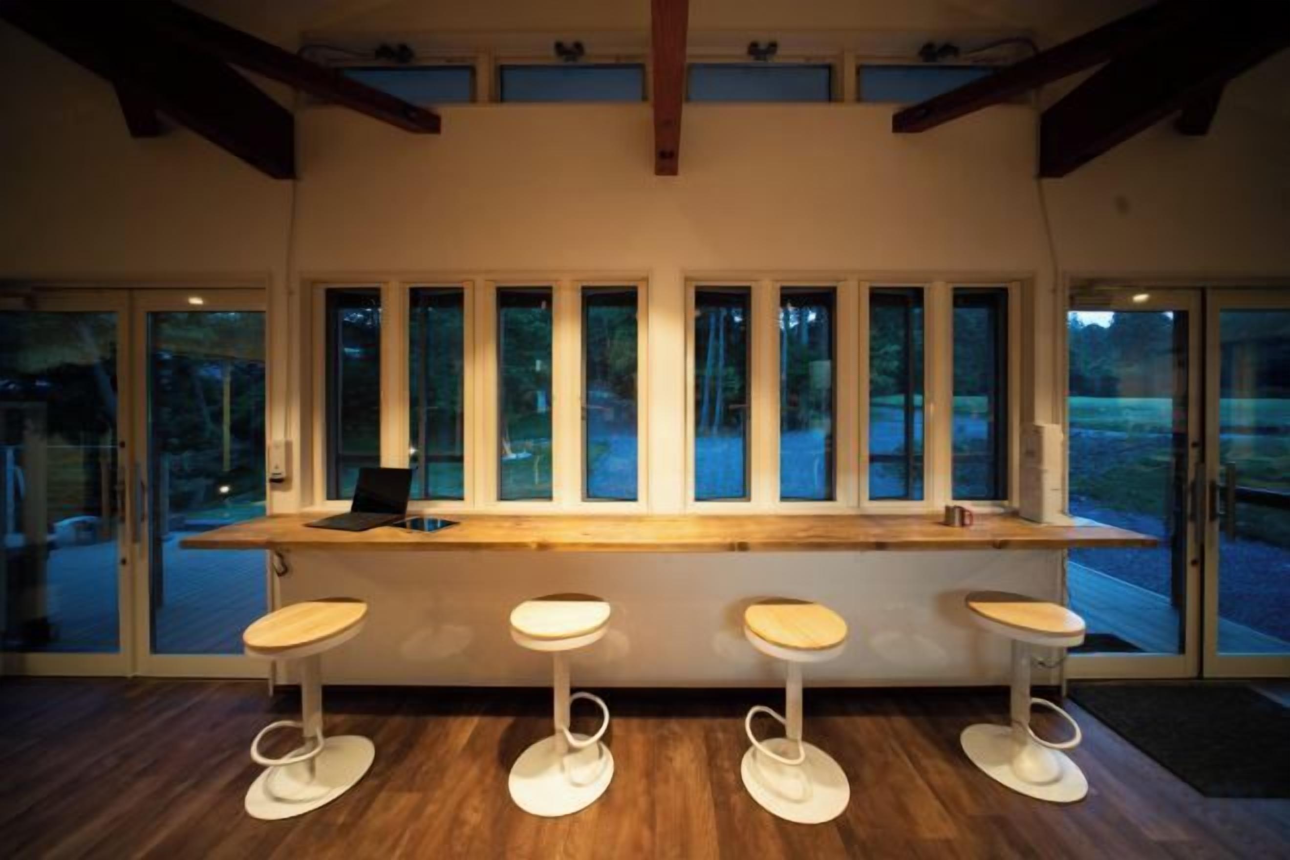 Zona de bar con mostrador de madera y cuatro taburetes, ventanas amplias y vistas al exterior.